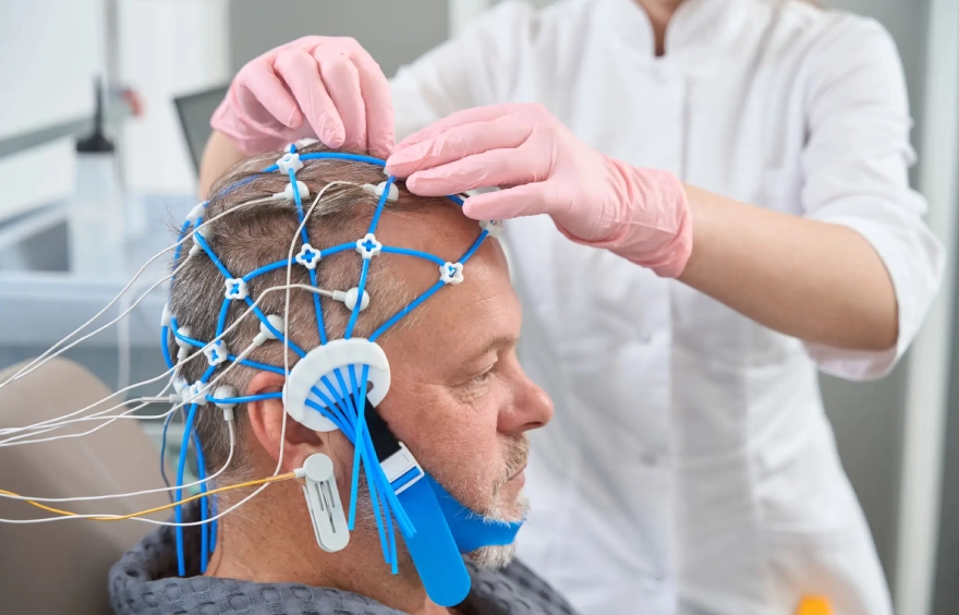 Man sitting in a chair with electrodes attached to his head, while a person wearing a dress