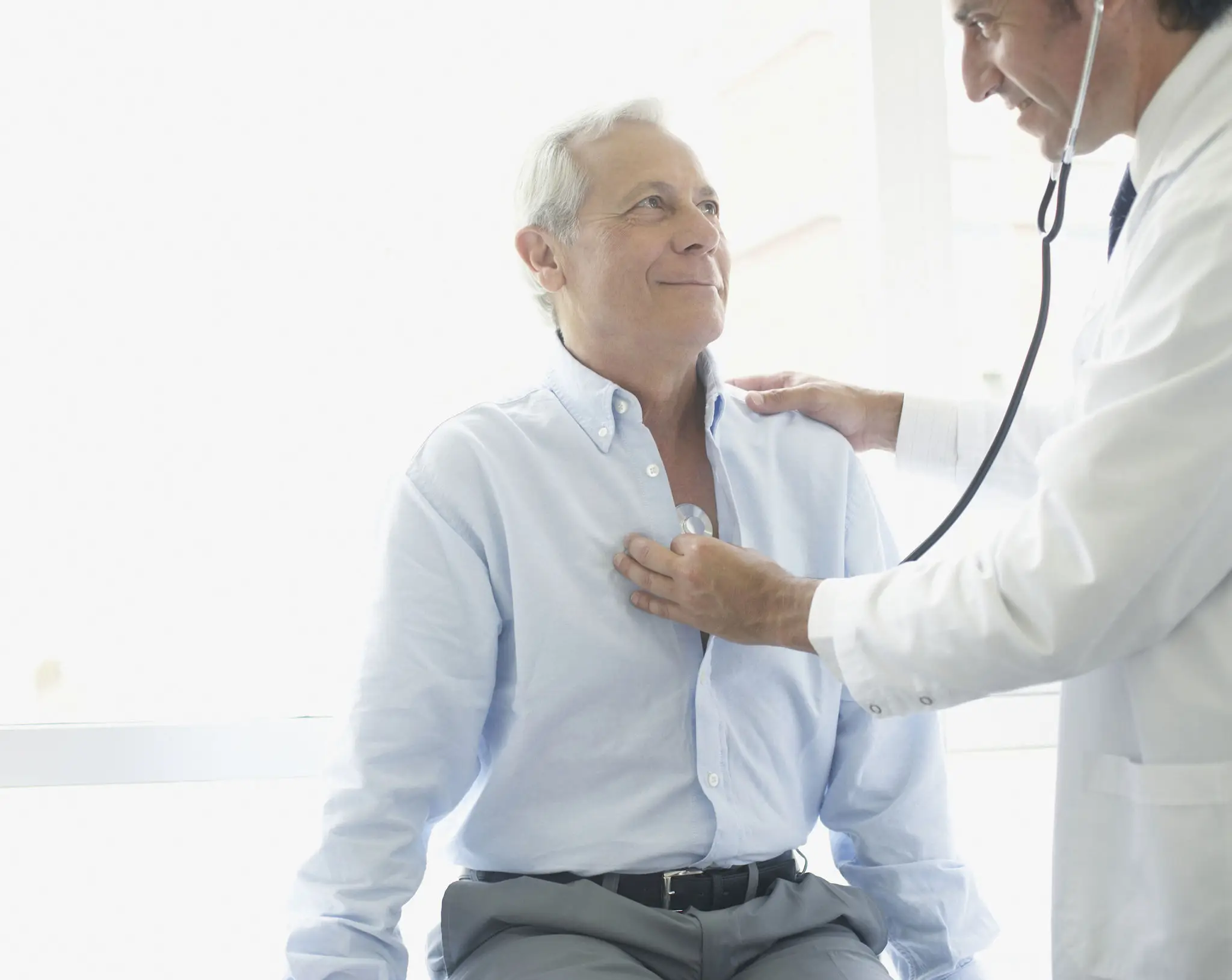 Doctor examining a patient's chest with a stethoscope while the patient is sitting in a chair