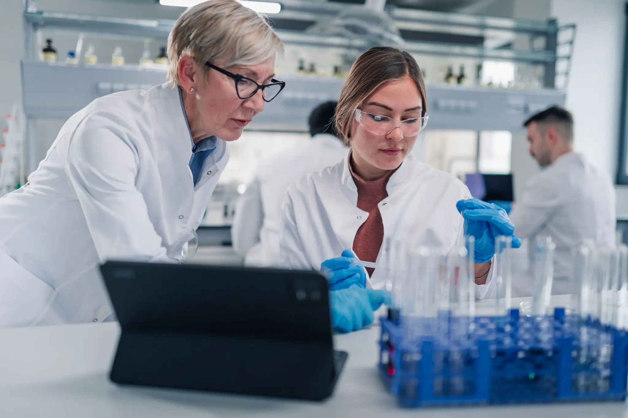 Two women in lab coats working on a laptop computer in a laboratory